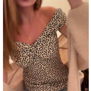Prickig offshoulder topp - Trendig offshoulder topp med svart och vit prickigt mönster. Toppen har en smickrande passform med knytning framtill. 