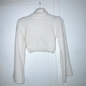 Vit fluffig croppad tröja - Säljer en supermjuk och fluffig vit croppad tröja med polokrage. Perfekt för att hålla sig varm och stilren under kyliga dagar. Tröjan har långa ärmar och en mysig textur. Passar även xs/s