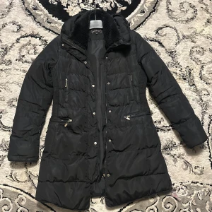 Svart dunjacka från Go Next - Snygg svart dunjacka från Go Next med pälskrage och dragkedja. Jackan har långa ärmar och flera praktiska fickor med dragkedjor. Perfekt för kyliga dagar.