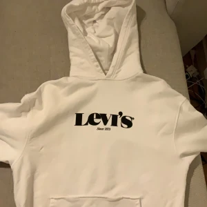 Vit hoodie från Levi's - Säljer en klassisk vit hoodie från Levi's med svart logotyp på framsidan. Den har en bekväm passform och en praktisk huva. Perfekt för en avslappnad stil.