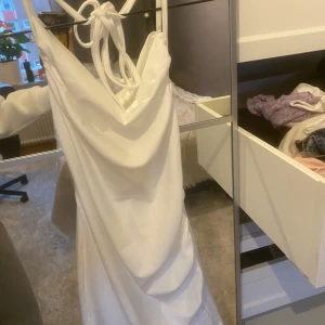 Vit klänning  - Elegant vit axelbandslös klänning med knytband i ryggen. Perfekt för sommarens festligheter med sin stilrena design och långa längd. 