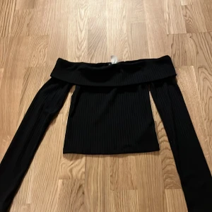Svart offshoulder topp från h&m i storlek xxs - Snygg svart offshoulder topp från h&m i ribbat material. Perfekt för en stilren look med långa ärmar och en elegant passform. Passar utmärkt till både jeans och kjol.