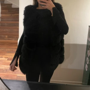 Svart pälsväst  - Snygg och elegant svart pälsväst från Chelsea i storlek XS. Perfekt för att ge din outfit en lyxig touch. Västen är mjuk och fluffig, vilket gör den både stilren och bekväm. Ett hål i fickan finns
