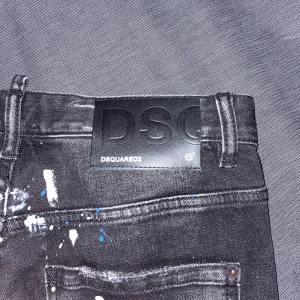 Svarta jeans från Dsquared2 - Snygga svarta jeans från Dsquared2 med coola slitningar och färgstänk i vitt och blått. Jeansen har en slim passform och är tillverkade i Italien. Perfekta för en trendig look! *priset kan diskuteras*