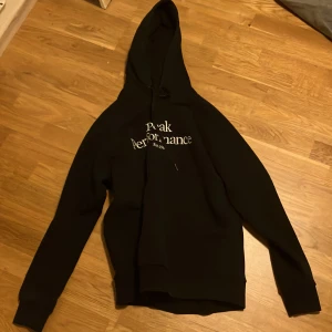 Svart hoodie från Peak Performance - Säljer en svart hoodie från Peak Performance med vit text på bröstet. Den har en klassisk design med huva och långa ärmar. Perfekt för en avslappnad stil.