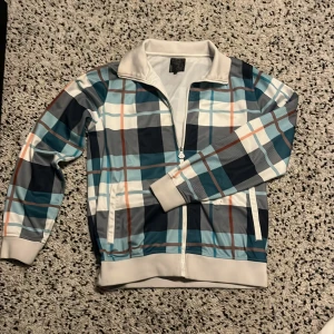 Rutig tracksuit från Warp - Snygg rutig jacka från Warp i blå, vit och grå med dragkedja framtill. Jackan har långa ärmar och en bekväm passform. Perfekt för en avslappnad stil.