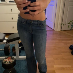 Blå jeans från J. Galt - Säljer ett par snygga blå jeans från J. Galt i storlek S. De är tillverkade av 99% bomull och 1% elastan, vilket gör dem både bekväma och stretchiga. Jeansen har en klassisk design med en straight passform och låg midja. Perfekta för vardagsbruk ell