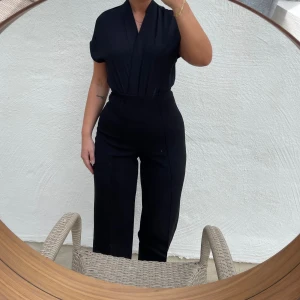 Svart byxdress - Säljer en elegant svart body med korta ärmar och v-ringad hals. Perfekt för både vardag och fest!
