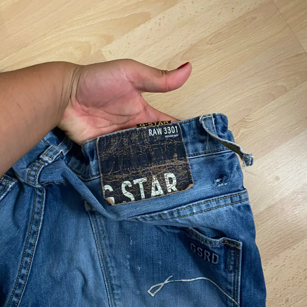 Säljer ett par snygga blå jeans från G-Star, modell RAW 3301. De har en klassisk femficksdesign med en cool sliten look. Perfekta för en avslappnad stil!. Jeans & Byxor.