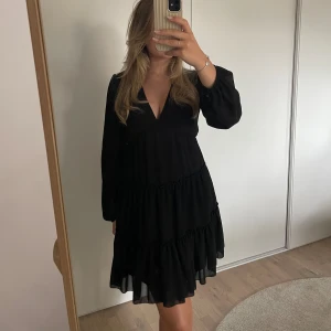 Svart festklänning  - Långärmad svart festklänning med volangkjol, djup v-ringning och långa ärmar. Använd en gång, nyskick. One size, jag bär vanligtvis storlek 36/S men klänningen är väldigt stretchig så den hade suttit lika bra på en som bär storlek XS-L