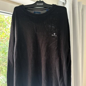 Svart tröja från GANT - Säljer en stilren svart tröja från GANT. Den är perfekt för både vardag och lite finare tillfällen. Använd en gång, den är som helt ny. L men sitter som M