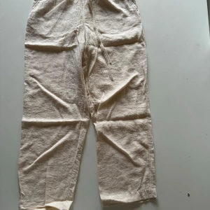 Beige linnebyxor med resårmidja - Säljer ett par bekväma och stilrena beige linnebyxor. De har en avslappnad passform med resår i midjan och dragsko för extra komfort. Perfekta för en avslappnad sommarlook eller en dag på stranden.