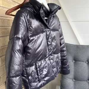 Svart vinter jacka - Intressekoll på en snygg och varm svart pufferjacka från 157. Jackan har en glansig yta och är perfekt för kalla dagar. Den har en huva och långa ärmar, vilket gör den idealisk för vinterväder. Jackan är i bra skick och redo för nya äventyr!