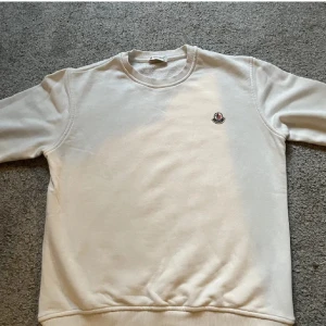 Vit tröja från Moncler - Säljer en stilren vit tröja från Moncler. Den har en klassisk design med rund hals och långa ärmar. Tröjan är i bra skick och perfekt för både vardag och lite finare tillfällen. Den har Monclers logga på bröstet som en snygg detalj.