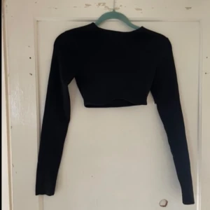 Svart croppad topp från NA-KD - Säljer en stilren svart croppad topp från NA-KD i storlek XS. Toppen har långa ärmar och är perfekt för en trendig look. Passar bra till både vardag och fest!