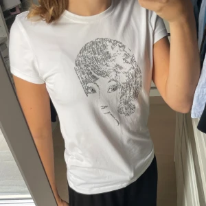 Vit t-shirt med tryck - En super fin vit t-shirt med ett ansikte på. Diamant detaljer finns även i trycket. Väldigt stretchigt material. Har nästan aldrig använts därför säljer jag den. 