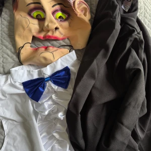 Halloween-kostymer och masker - Säljer en samling av Halloween-kostymer och masker. Första kostymen inkluderar en skrämmande mask med sprickor och en vit skjorta med en blå fluga. Andra kostymen är en paramedic-outfit i grönt med blodstänk, komplett med handskar, mask och accessoarer. Det finns också tre olika vita masker, varav en har röda läppar och en annan är en klassisk skräckmask.