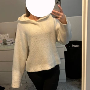 Vit stickad hoodie - Mysig och varm vit hoodie i stickat-material. Perfekt för kyliga dagar med sin avslappnade passform och långa ärmar. Den har en bekväm huva som ger extra värme och stil.