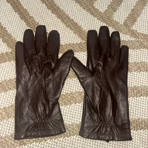 Bruna skinnhandskar - Säljer ett par snygga bruna skinnhandskar i nyskick. De är perfekta för hösten och har en stilren design med elastisk detalj vid handleden för bättre passform. Handskarna är mjuka och bekväma, det är också bra att veta att de är ganska små)