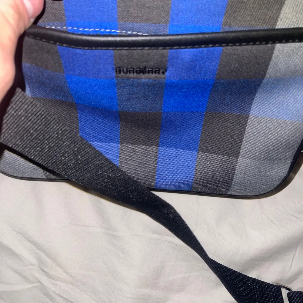 Säljer en snygg burberry axelväska med ett rutigt mönster i blått och grått. Väskan har en justerbar axelrem och en dragkedja upptill. Perfekt för både vardag och fest! 👜. Väskor.