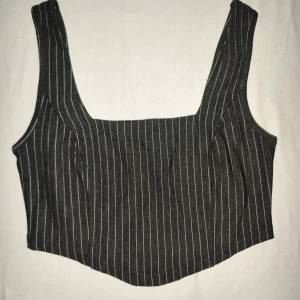 Randig svart korsett topp från Stories - Säljer en snygg svart korsett från Stories i storlek XS. Den har ett stilrent randigt mönster och är perfekt för både vardag och fest. Passformen är tight och den är tillverkad i ett bekvämt material. Perfekt att matcha med höga jeans eller en kjol!