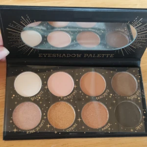 Ögonskuggspalett från LASplash Cosmetics - Säljer en magisk ögonskuggspalett från LASplash Cosmetics med åtta fantastiska nyanser: Selenite, Sunstone, Aragonite, Tiger's Eye, Rose Quartz, Citrine, Amber och Onyx. Perfekt för att skapa både vardagliga och dramatiska looks. Paletten har en elegant design med mystiska symboler i guld på svart bakgrund.