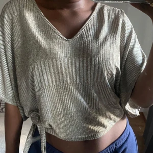 Glittrig guld topp - Säljer en superfin glittrig guld topp med v-ringning och korta ärmar. Toppen har en snygg knytning i sidan som ger en cool look. Perfekt för festliga tillfällen! 💞💞