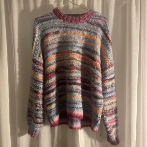 Färgglad stickad tröja från Bik Bok - Säljer en supermysig och färgglad stickad tröja från Bik Bok. Den har ett randigt mönster i olika nyanser av rosa, blått, orange och grått. Perfekt för att liva upp höst- och vintergarderoben! Tröjan är långärmad och har en skön passform som är lite oversized. Perfekt för kyliga dagar när du vill vara både varm och stilren.