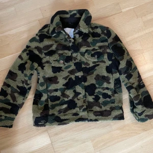 Samsoe Samsoe Jacka  - ”Colly Jacket” från Samsoe Samsoe. Jacka i teddy material med camouflage mönster. Få tecken på användning i tyget inkluderade bild med exempel! 