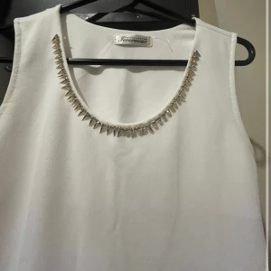Vit ärmlös klänning med pärldetaljer - Säljer en vit topp/miniklänning från Glamorous. Den är ärmlös och har en snygg pärldetalj runt halsringningen som ger en extra touch av glamour. Perfekt för sommarens fester eller en elegant middag. Klänningen är i nyskick och har en normal passform.