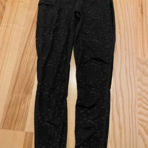 Svarta mönstrade leggings från Newbody - Säljer ett par gröna tights från Newbody. Perfekta för träning eller en avslappnad dag. Materialet är stretchigt och bekvämt, vilket gör dem idealiska för olika aktiviteter. De har en hög midja för extra komfort och mesh i knävecken. 