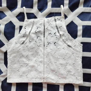 Vit spetslinne - Säljer en superfin vit spetslinne med blommigt mönster. Den är ärmlös och har smala axelband, perfekt för sommardagar eller festliga tillfällen. Toppen är croppad och ger en söt och romantisk look. Passar perfekt till både jeans och kjol!