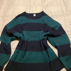 Randig stickad tröja i grönt och svart - Säljer en supermysig stickad tröja med breda ränder i grönt och mörkblått. Den har en avslappnad passform och långa ärmar, perfekt för kyliga dagar. Tröjan är i storlek M och passar både till jeans och kjol. Perfekt för höst och vinter!