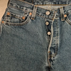 Levi's jeans i blå denim - Klassiska Levi's jeans i blå denim med hög midja och knappgylf. W28 men skulle säga att de snarare skulle passa ngn som vanligtvis har W26-27.