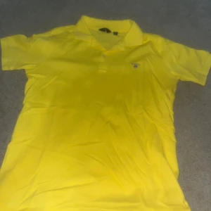 Gul kortärmad pikétröja från Gant - Säljer en solgul kortärmad pikétröja från Gant. Perfekt för sommardagar med sin fräscha färg och klassiska design. Tröjan har en liten broderad logga på bröstet och en bekväm passform. Priset kan diskuteras! 