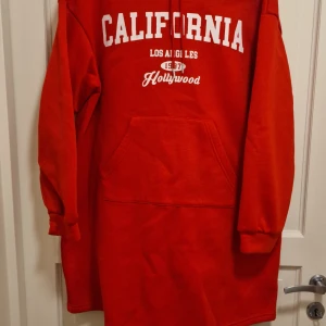 Röd hoodie från Shein - Säljer en röd hoodie från Shein med texten 'California Los Angeles Hollywood' i vitt. Den har en stor ficka framtill och långa ärmar. Perfekt för en avslappnad stil.