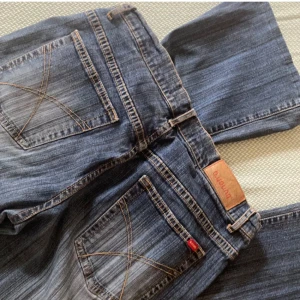 Blå bootcut jeans från b.young - Säljer ett par snygga blå bootcut jeans från b.young. De har en klassisk femficksdesign och slitna detaljer på framsidan. Perfekta för en avslappnad stil.