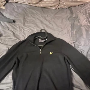 Svart tröja med dragkedja från Lyle & Scott - Snygg svart tröja från Lyle & Scott med halv dragkedja och deras ikoniska gula logga på bröstet. Perfekt för en stilren look. Nypris:499 Skick 9/10 