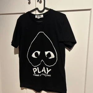Svart t-shirt från Comme des Garçons - Snygg svart t-shirt från Comme des Garçons med det ikoniska PLAY-trycket i vitt framtill. Perfekt för en stilren och modern look.