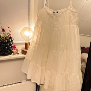 Vit klänning - Vit klänning med tunna axelband. Den har en luftig design med volanger. 