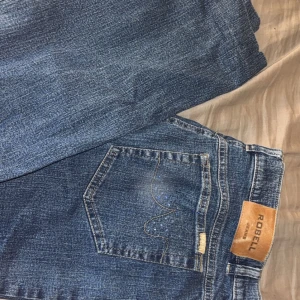 Blå jeans från Robell - Snygga blå jeans från Robell med klassisk femficksdesign. De har en rak passform och är perfekta för en avslappnad stil. Jeansen har en knapp och dragkedja framtill.
