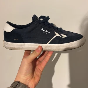 Blå sneakers från Pepe Jeans - Snygga blå sneakers från Pepe Jeans med vita detaljer och snörning. Skorna har en klassisk design med en vit sula och märkeslogga på sidan. Perfekta för en avslappnad stil.