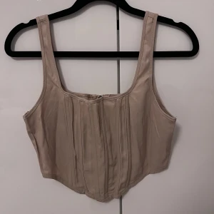 Beige korsett från Missguided - Snygg beige korsett från Missguided med dragkedja framtill. Perfekt för att ge en stilren look. Passar bra till både jeans och kjol.