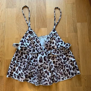 Leopardmönstrad blus - Snygg leopardmönstrad linne med smala axelband och volangdetaljer. Perfekt för en trendig look.