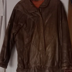 Brun skinnjacka med mönstrat foder - Säljer en brun skinnjacka med ett unikt mönstrat foder. Jackan har en klassisk krage och stängs med dragkedja. Perfekt för höst och vår.