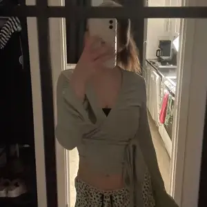 Snygg grå omlottopp med långa ärmar och knytning i midjan. Perfekt för en stilren look.💕