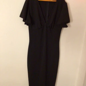 Svart klänning med v-ringning - Elegant svart klänning med djup v-ringning och korta ärmar. Perfekt för en stilren look.