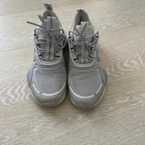 Grå sneakers från Adidas - Snygga grå sneakers från Adidas med klassiska tre ränder på sidan. Skorna har snörning och en bekväm sula för extra komfort. Perfekta för en sportig look.