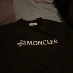 Svart tröja från Moncler - Snygg svart tröja från Moncler med deras ikoniska logga i vitt på bröstet. Perfekt för en stilren look.