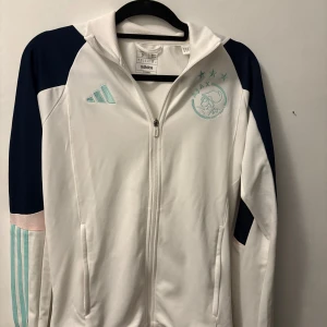 Vit och blå Ajax kofta - Snygg vit blå Ajax kofta. Säljer för det blev inte så mycket användning av den. Köpt i Amsterdam på Ajax arena för 180€ vilket motsvarar ungefär 2000kr. Mitt pris 1000. Storlek S men skulle också passa M. Pris kan diskutera!😊